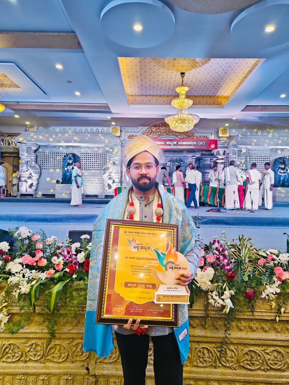 Dr. Adarsh holding a framed certificate and trophy at a felicitation ceremony